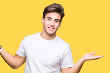 Gülen iki elle gösterilen açık avuç içi, sunma ve karşılaştırma ve denge reklam arka plan üzerinde beyaz t-shirt giyen genç yakışıklı adam izole
