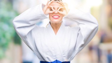 Üzerinde karate kimono üniforma giyen genç güzel kadın dilini, parmaklarının arasından baktığını yapışmasını dürbün gibi ok jest yapıyor arka plan izole. Deli ifade.