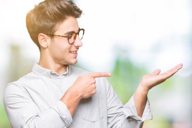 Hayret ve el ile sunulması ve parmak ile işaret ederken kameraya gülümseyen izole arka plan üzerinde gözlük takan genç yakışıklı adam.