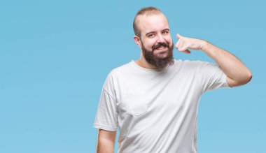 İşin gülümseyen izole arka plan üzerinde rahat t-shirt giyen genç beyaz hipster adam telefon hareketi ile el ve parmak telefonda konuşuyor gibi. Kavramları iletişim.