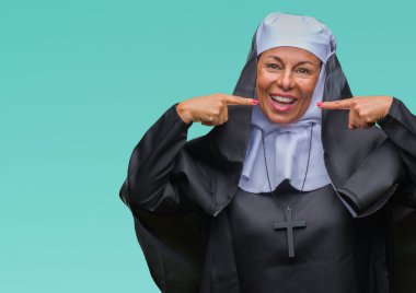 Orta yaş üst düzey Hıristiyan Katolik Rahibe kadın kendinden emin gösterilen ve işaret parmakları diş ve ağız ile gülümseyen izole arka plan yüzünden. Sağlık kavramı.