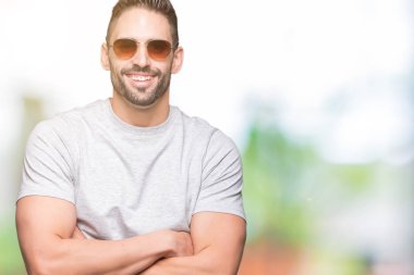 Yakışıklı delikanlı üzerinde güneş gözlüğü takıyor mutlu yüz ile gülümseyerek kameraya seyir silah geçti arka plan izole. Olumlu bir kişi.