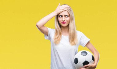 Futbol topu kafa üzerinde el ile vurguladı izole arka plan üzerinde tutan genç güzel sarışın kadın şok utanç ve sürpriz suratla, öfkeli ve sinirli. Korku ve hata için üzgün.