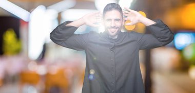 Genç Hıristiyan rahip izole arka plan üzerinde rahatlatıcı ve kollar ve eller baş ve boyun, mutlu gülümseyerek arkasında ile germe