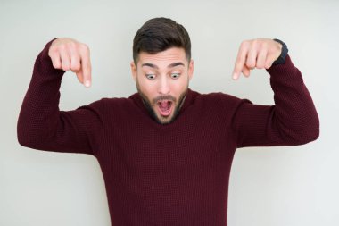 Bir kazak izole üzerinde giyen genç yakışıklı adam arka plan işaretleme aşağı reklam, sürpriz yüz ve açık ağız gösterilen parmakları ile