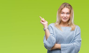 Kameraya bakarak yan el ve parmak ile işaret yüzünde kocaman bir gülümseme ile izole arka plan üzerinde kış kazak giyen genç beyaz kadın.