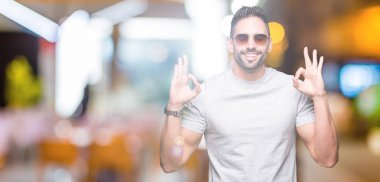 Genç yakışıklı adam giyen güneş gözlüğü izole arka plan üzerinde dinlenmek ve gülümseyen gözlerle parmak ile meditasyon jest yapıyor kapalı. Yoga kavramı.