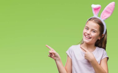 Paskalya bunny kulaklar gülümseyen ve iki elleri ve parmakları ile tarafına işaret kamera bakarak izole arka plan üzerinde giyen genç güzel kız.