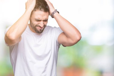 Genç adam giyiyor rahat beyaz t-shirt çünkü umutsuz ve stresli baş ağrısı acı izole arka plan üzerinde ağrı ve migren. Ellerini kafasına.