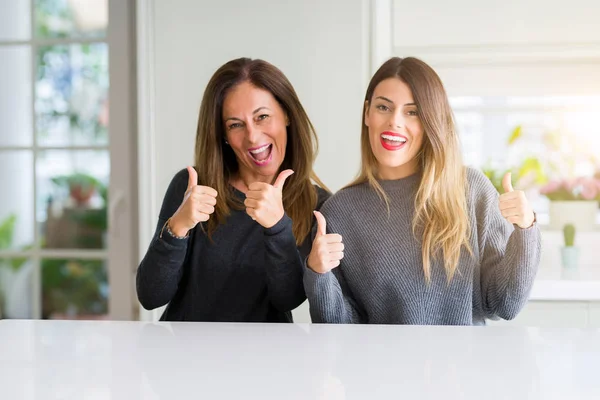 Beautiful family of mother and daughter together at home success sign doing positive gesture with hand, thumbs up smiling and happy. Looking at the camera with cheerful expression, winner gesture.
