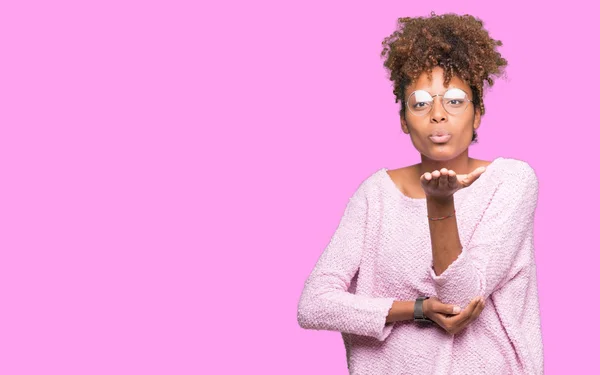 Beautiful young african american woman wearing glasses over isolated background looking at the camera blowing a kiss with hand on air being lovely and sexy. Love expression.