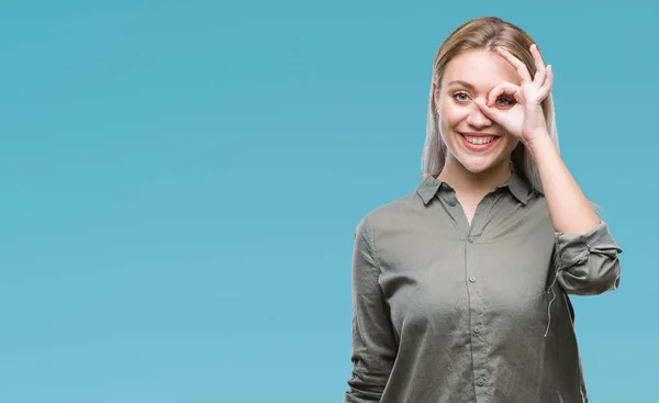 Young blonde business woman over isolated background doing ok gesture with hand smiling, eye looking through fingers with happy face.