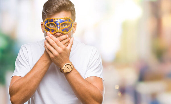 Young handsome man wearing carnival mask over isolated background shocked covering mouth with hands for mistake. Secret concept.