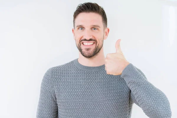 Stock image Young handsome man wearing casual sweater over isolated background doing happy thumbs up gesture with hand. Approving expression looking at the camera with showing success.