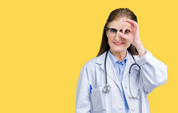 中年成熟的医生妇女穿着医疗外套在孤立的背景做确定的手势与手微笑 眼睛通过手指看与快乐的脸 — 图库照片