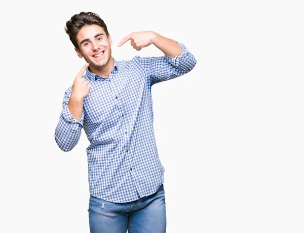 Genç yakışıklı iş adamı kendine güvenen gösterilen ve işaret parmakları diş ve ağız ile gülümseyen izole arka plan üzerinde. Sağlık kavramı.