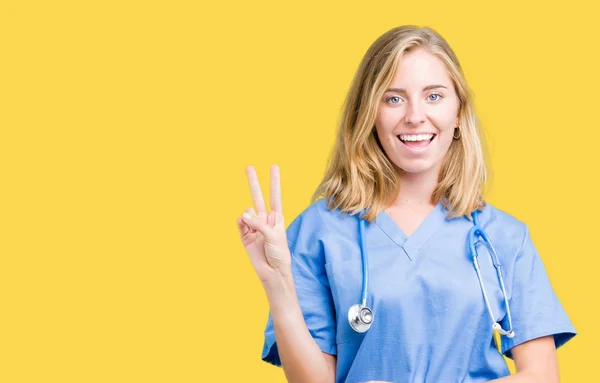 美丽的年轻医生妇女穿着医疗制服在孤立的背景微笑着 高兴的脸眨眼在相机做胜利的标志 — 图库照片