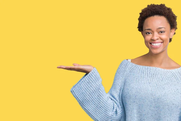 Neşeli sunulması ve kameraya bakarak avucunun ile işaret gülümseyen izole arka plan üzerinde bir kazak giyen genç güzel Afrikalı-Amerikalı kadın.