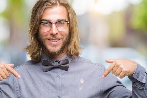 Young handsome man with long hair wearing bow tie over isolated background looking confident with smile on face, pointing oneself with fingers proud and happy.