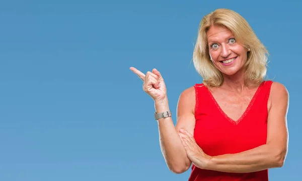 Middle age blonde woman over isolated background with a big smile on face, pointing with hand and finger to the side looking at the camera.