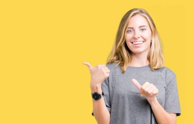 Güzel genç kadın üzerinde büyük boy rahat t-shirt giyen izole arka plan emin gülümseyen arkasından el ve kadar başparmak ile işaret