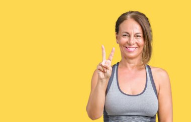 Güzel orta yaş kadın giyiyor spor giyim gösterilen ve parmakları ile işaret izole arka plan üzerinde kendinden emin ve mutlu gülümseyerek iken ikincisi.