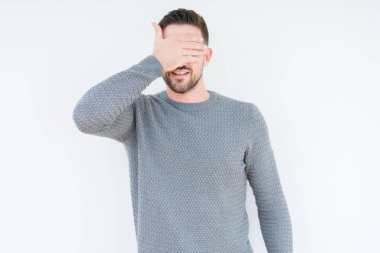 Genç yakışıklı adam gülümsüyor ve gözleri için sürpriz kapsayan yüz el ile gülüyor izole arka plan üzerinde rahat kazak giyiyor. Kör kavramı.