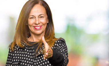 Tebrik ve konuksever dost sunan karşılıklı gülümseyen moda ceket giyen güzel orta yaş kadın. Başarılı iş.