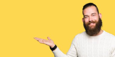 Neşeli sunulması ve kameraya bakarak avucunun ile işaret gülümseyen kış kazak giyen genç hipster adam.