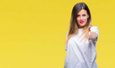 Genç güzel kadın rahat beyaz t-shirt üzerine izole arka plan tebrik ve davet edici olarak gülümseyen dostu sunan el sıkışma. Başarılı iş.