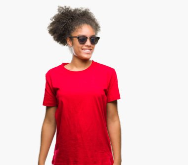 Genç afro Amerikalı kadın uzak tarafına yüzünde, doğal ifade gülümseme ile seyir izole arka plan üzerinde güneş gözlüğü takıyor. Kendine güvenen gülüyor.