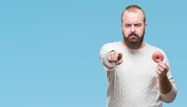 Kamera ve size parmak ile işaret izole arka plan üzerinde genç beyaz hipster man yemek tatlı çörek, el işareti, pozitif ve kendinden emin bir jest ön