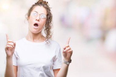 İzole arka plan üzerinde gözlük güzel genç esmer kıvırcık saçlı kız hayran ve yukarıya bakıp parmakları ile işaret şaşırttı ve silah kaldırdı.