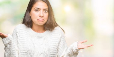 İzole arka plan clueless ve şaşkın bir ifadeyle kollar ve eller kaldırdı üzerinde kış kazak giyen genç güzel Arap kadın. Şüphe kavramı.