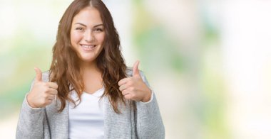 Artı boyutu genç kadın güzel izole arka plan başarı işareti el ile pozitif jest yapıyor üzerinde kış ceket başparmak gülümseyen ve mutlu. Neşeli bir ifadeyle, kazanan jest kameraya bakıyor.