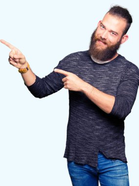 Genç sarışın adam rahat kazak giyen gülümseyen ve iki elleri ve parmakları ile tarafına işaret kamera bakıyor.