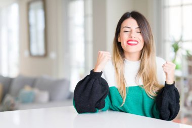 Zafer kutluyor gülümseyen başarı kollarını kaldırdı için evde kış kazak giyen genç güzel kadın heyecan. Kazanan kavramı.