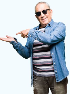 Denim ceket ve hayrete ve el ile sunulması ve parmak ile işaret ederken kameraya gülümseyen güneş gözlüğü takan yakışıklı komuta sizde.