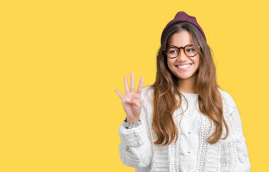 Genç güzel esmer hipster kadın gözlük ve kış şapka gösterilen ve parmakları ile işaret izole arka plan üzerinde dört kendinden emin ve mutlu gülümseyerek iken numara.