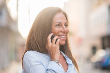 Güzel orta yaş İspanyol kadın ayakta yüzünde gülümseme ile sokağın Evet. Güneşli bir günde kendine güvenen ve neşeli gülen üzerinden yürüyüş.