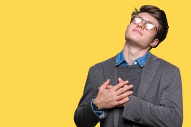 Göğüs kapalı gözlerle ellerinde ve yüzünde minnettar jest ile gülümseyen izole arka plan üzerinde gözlük takan genç yakışıklı iş adamı. Sağlık kavramı.