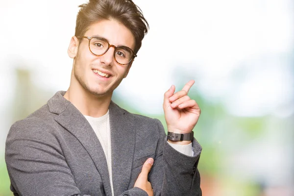 Yüzünde kocaman bir gülümseme ile izole arka plan üzerinde gözlük takan genç iş adamı kameraya bakarak yan el ve parmak ile işaret.