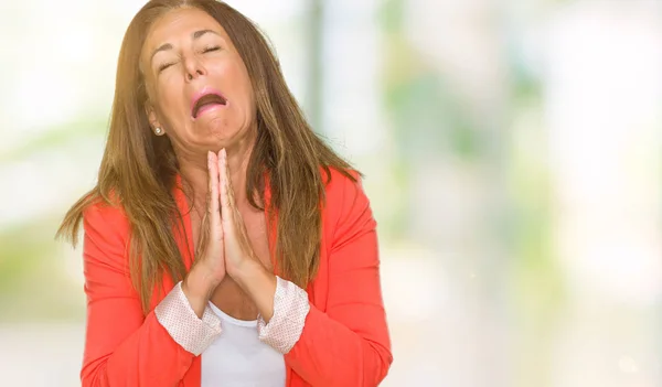 Beautiful middle age business adult woman over isolated background begging and praying with hands together with hope expression on face very emotional and worried. Asking for forgiveness. Religion concept.