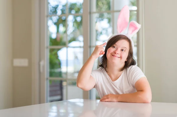 Down syndrome woman at home wearing easter rabbit ears very happy pointing with hand and finger