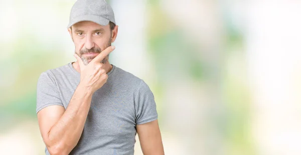 Handsome middle age hoary senior man wearing sport cap over isolated background looking confident at the camera with smile with crossed arms and hand raised on chin. Thinking positive.