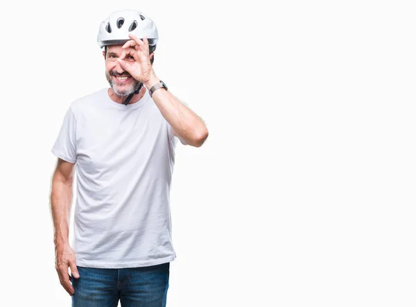 Middle age senior hoary cyclist man wearing bike safety helment isolated background doing ok gesture with hand smiling, eye looking through fingers with happy face.