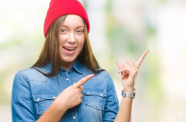 年轻的高加索美丽的女人穿着羊毛帽在孤立的背景微笑着 看着相机指向与两个手和手指的一侧 — 图库照片