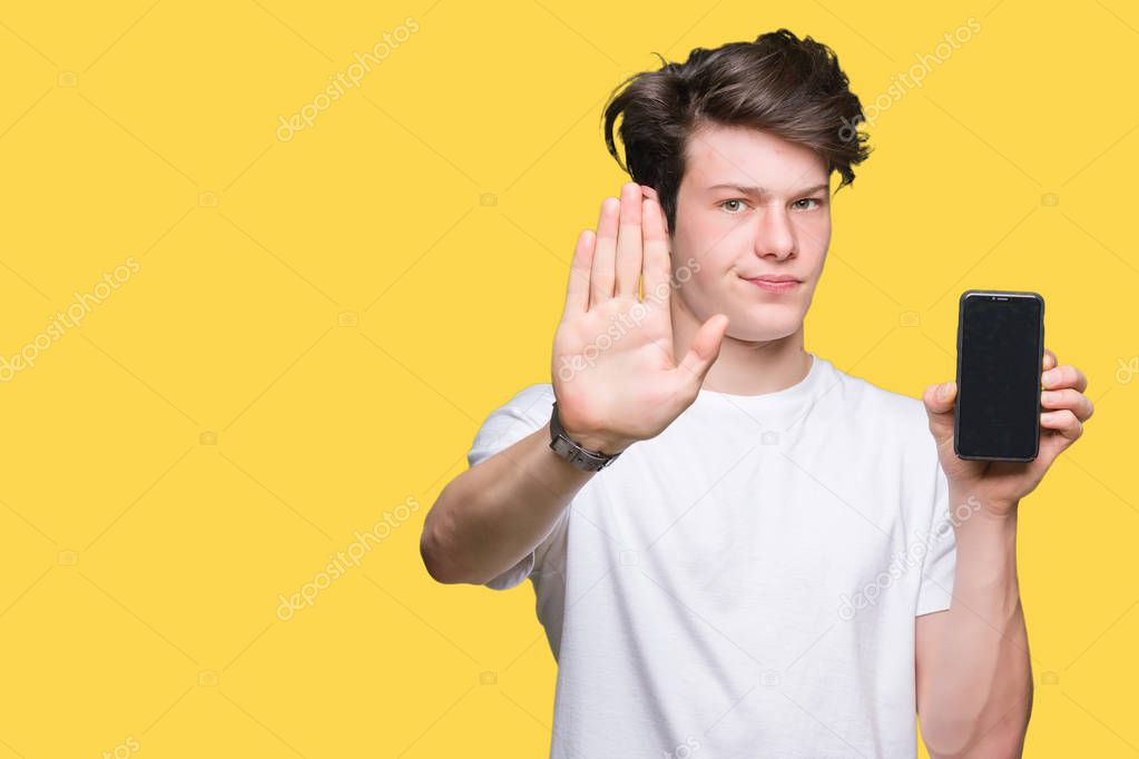 Young man showing smartphone screen over isolated background with open hand doing stop sign with serious and confident expression, defense gesture
