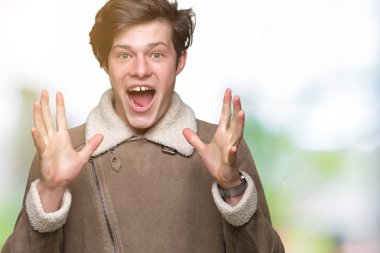 Üzerinde kış ceket giyen genç yakışıklı adam deli kutluyor arka plan izole ve başarı için kaldırdı kollarını açarak hayrete ve heyecanlı çığlık gözleri açık. Kazanan kavramı