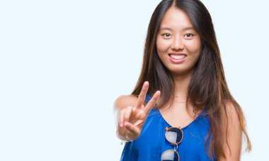 Genç Asyalı kadın parmaklarını zafer işareti yaparken gösterilen kamera seyir gülümseyen izole arka plan üzerinde. İki numaralı.